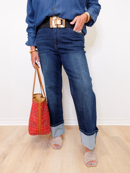 Person wearing blue jeans and a denim shirt, holding a red handbag against a white background