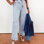 Person wearing light blue jeans and a red patterned top, holding a denim jacket.