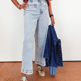 Person wearing light blue jeans and a red patterned top, holding a denim jacket.