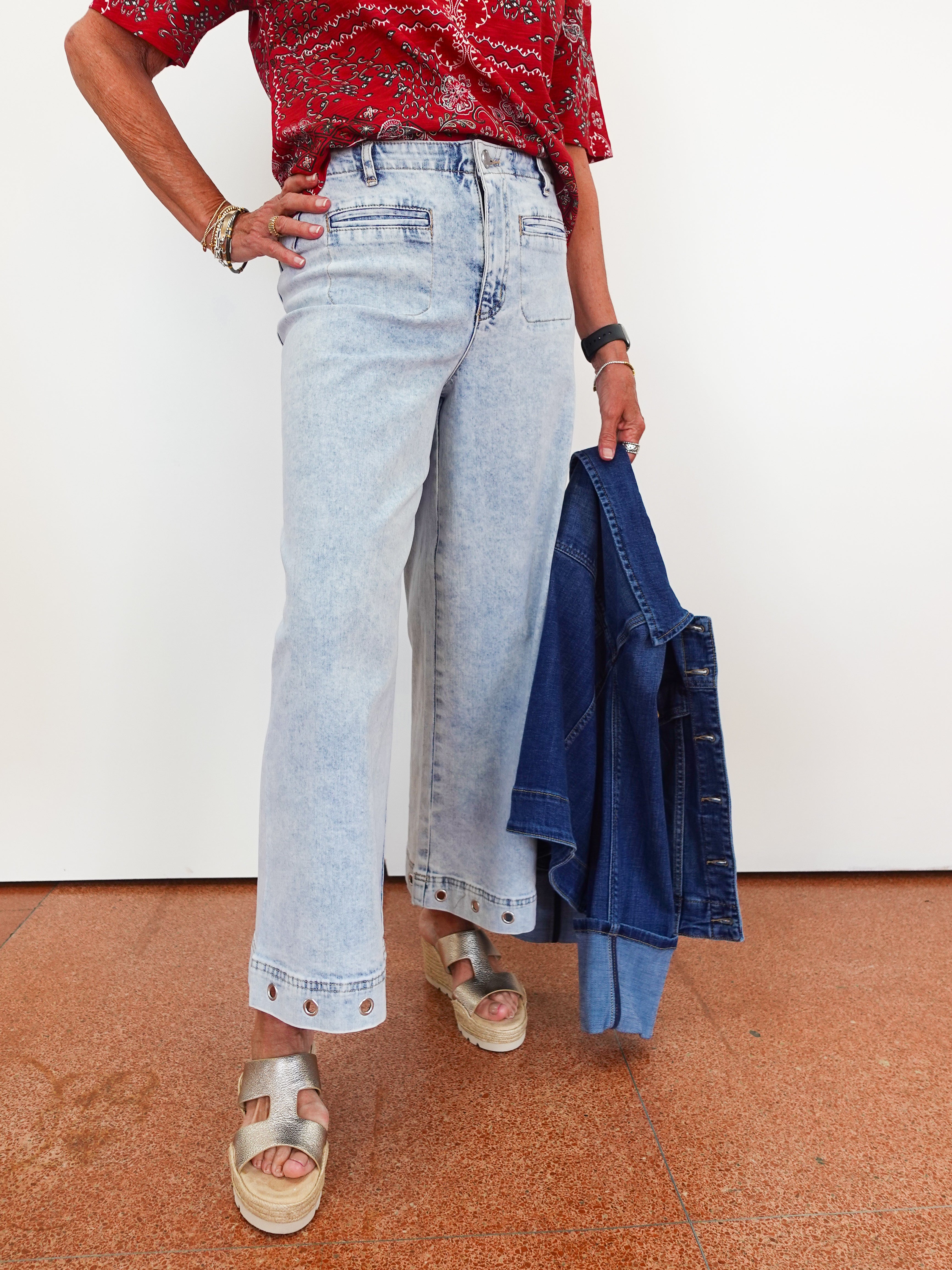 Person wearing light blue jeans and a red patterned top, holding a denim jacket.