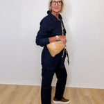 Person wearing a navy outfit with a beige bag against a white wall