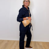 Person wearing a navy outfit with a beige bag against a white wall