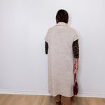 Person wearing a long beige cardigan with leopard print sleeves against a white wall.