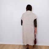 Person wearing a long beige cardigan with leopard print sleeves against a white wall.