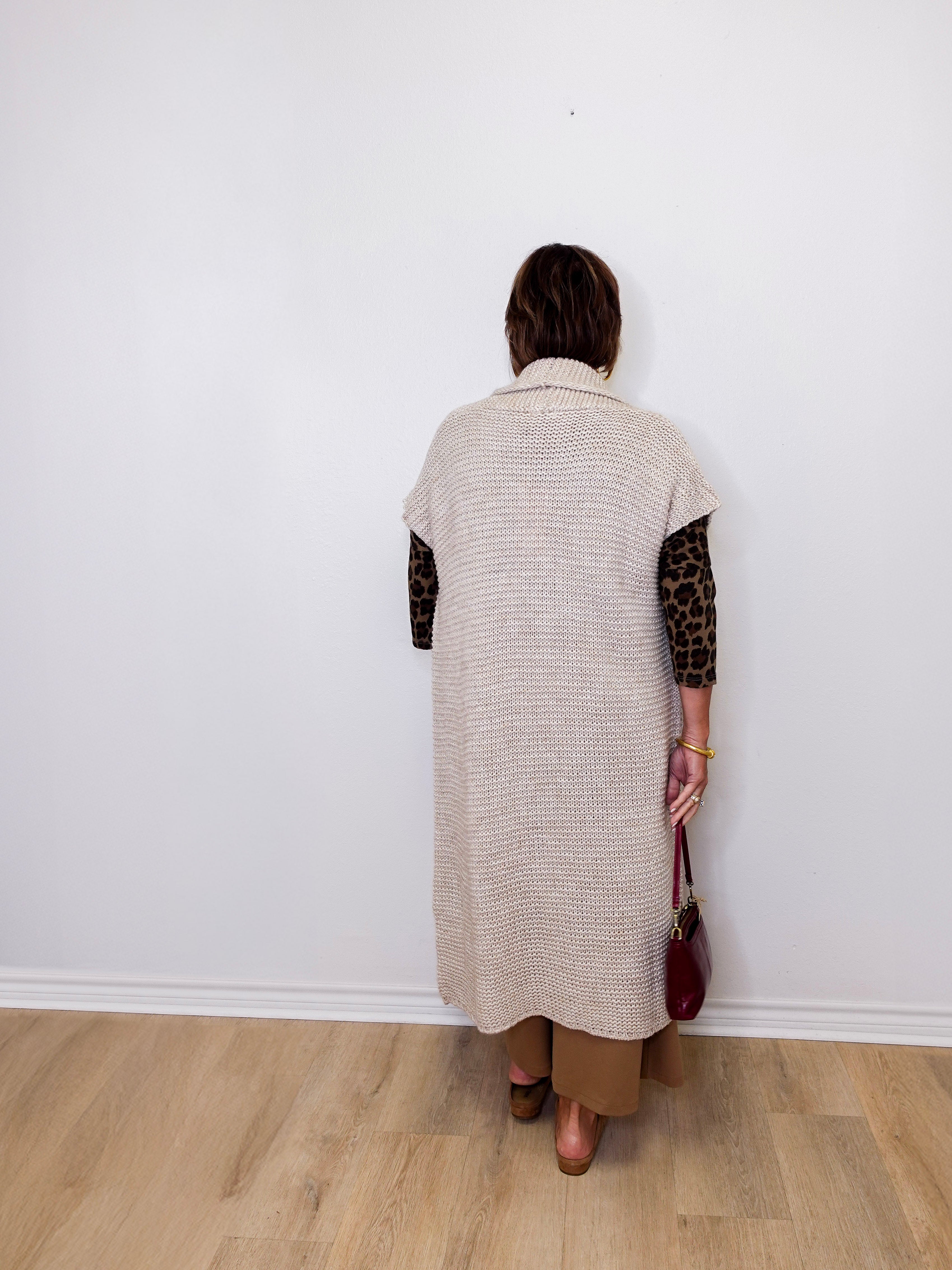Person wearing a long beige cardigan with leopard print sleeves against a white wall.