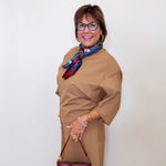 Woman wearing a brown outfit with a scarf and holding a red handbag against a white background