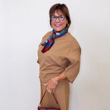 Woman wearing a brown outfit with a scarf and holding a red handbag against a white background