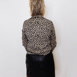 Person wearing a leopard print shirt and black skirt against a white wall.