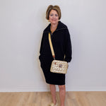 Woman in black outfit with gold handbag against a white wall