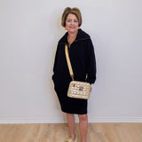 Woman in black outfit with gold handbag against a white wall