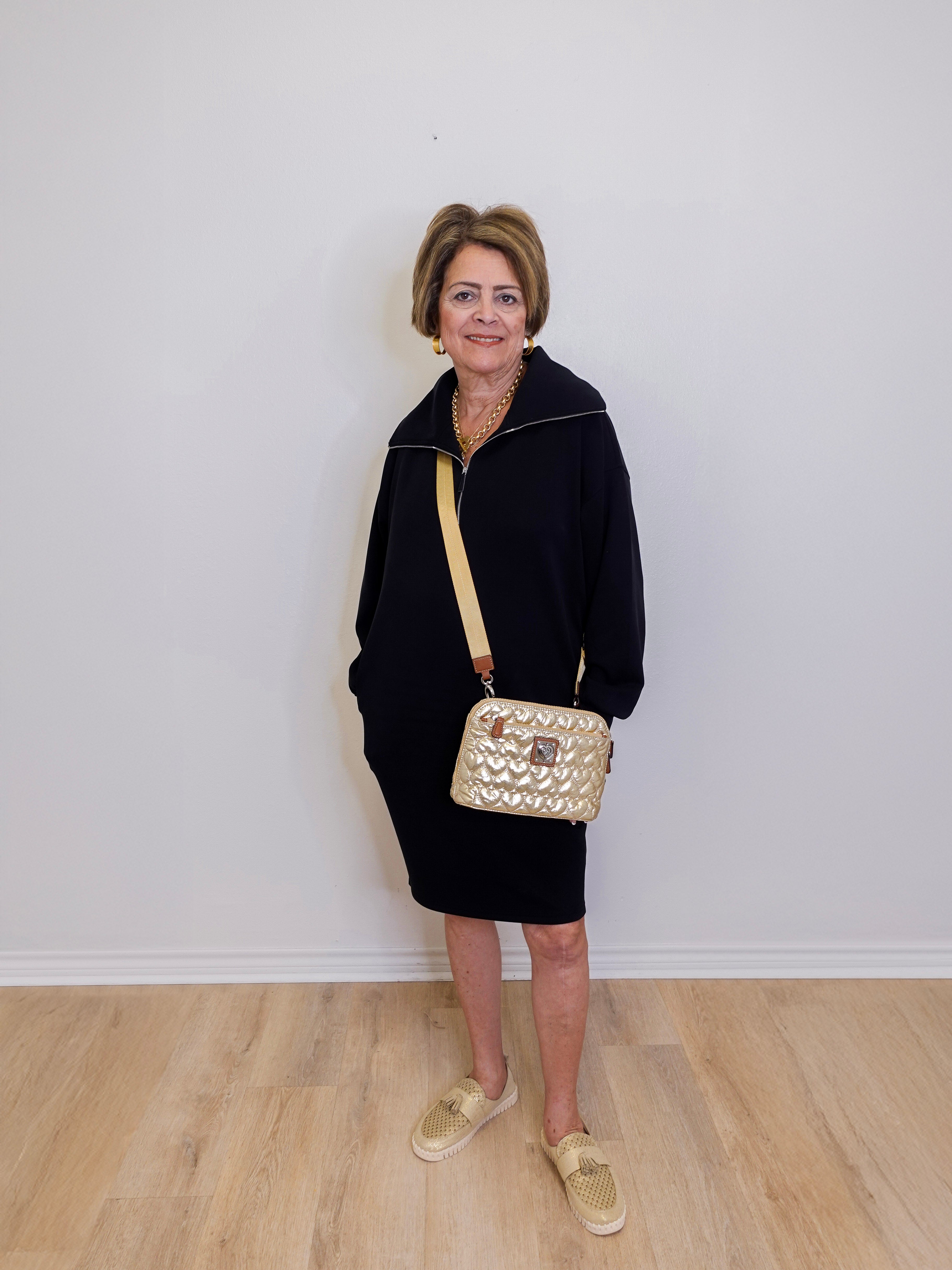 Woman in black outfit with gold handbag against a white wall