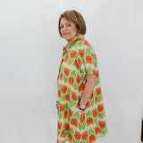 Woman wearing a colorful patterned dress against a white wall.