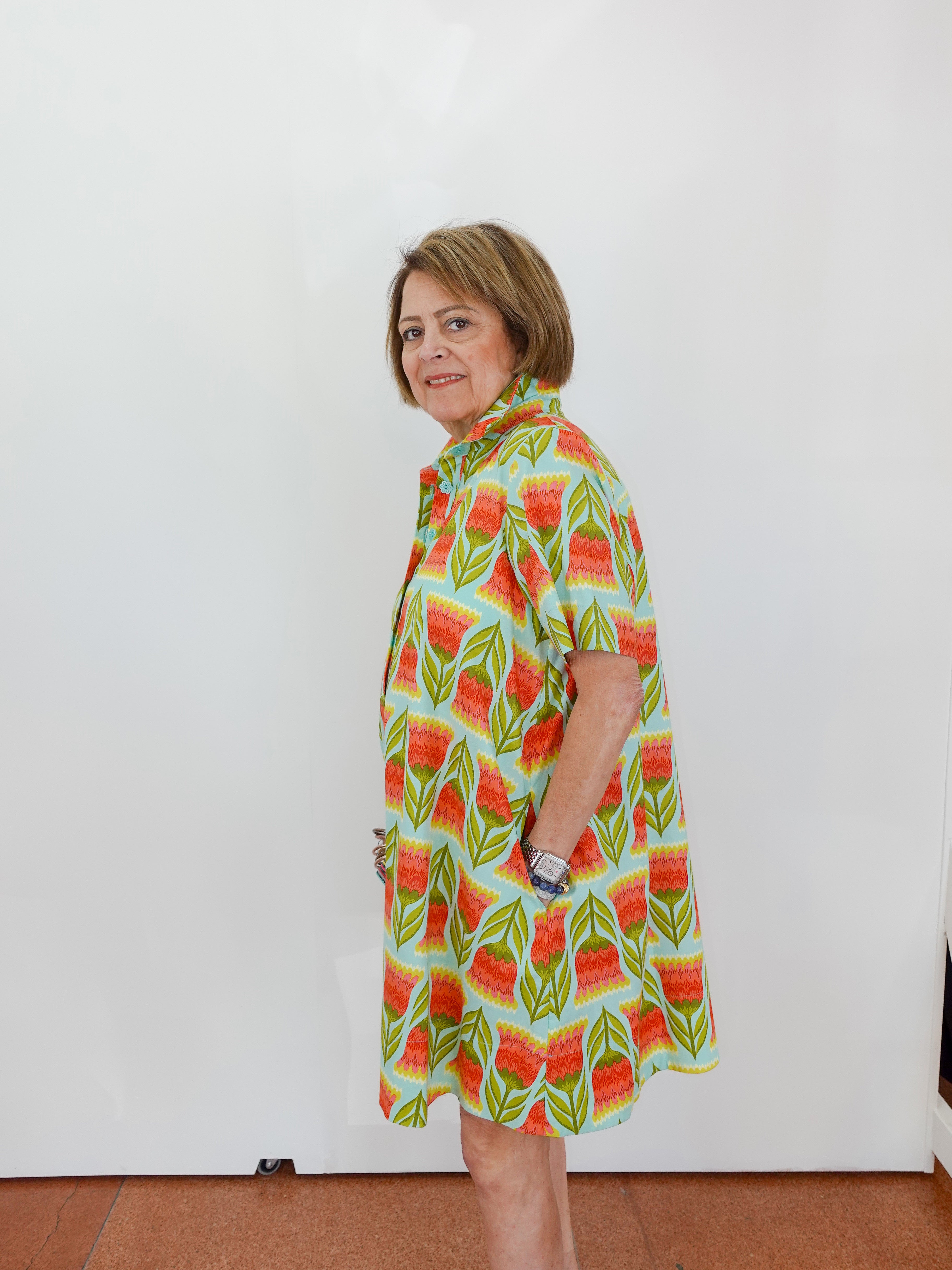 Woman wearing a colorful patterned dress against a white wall.