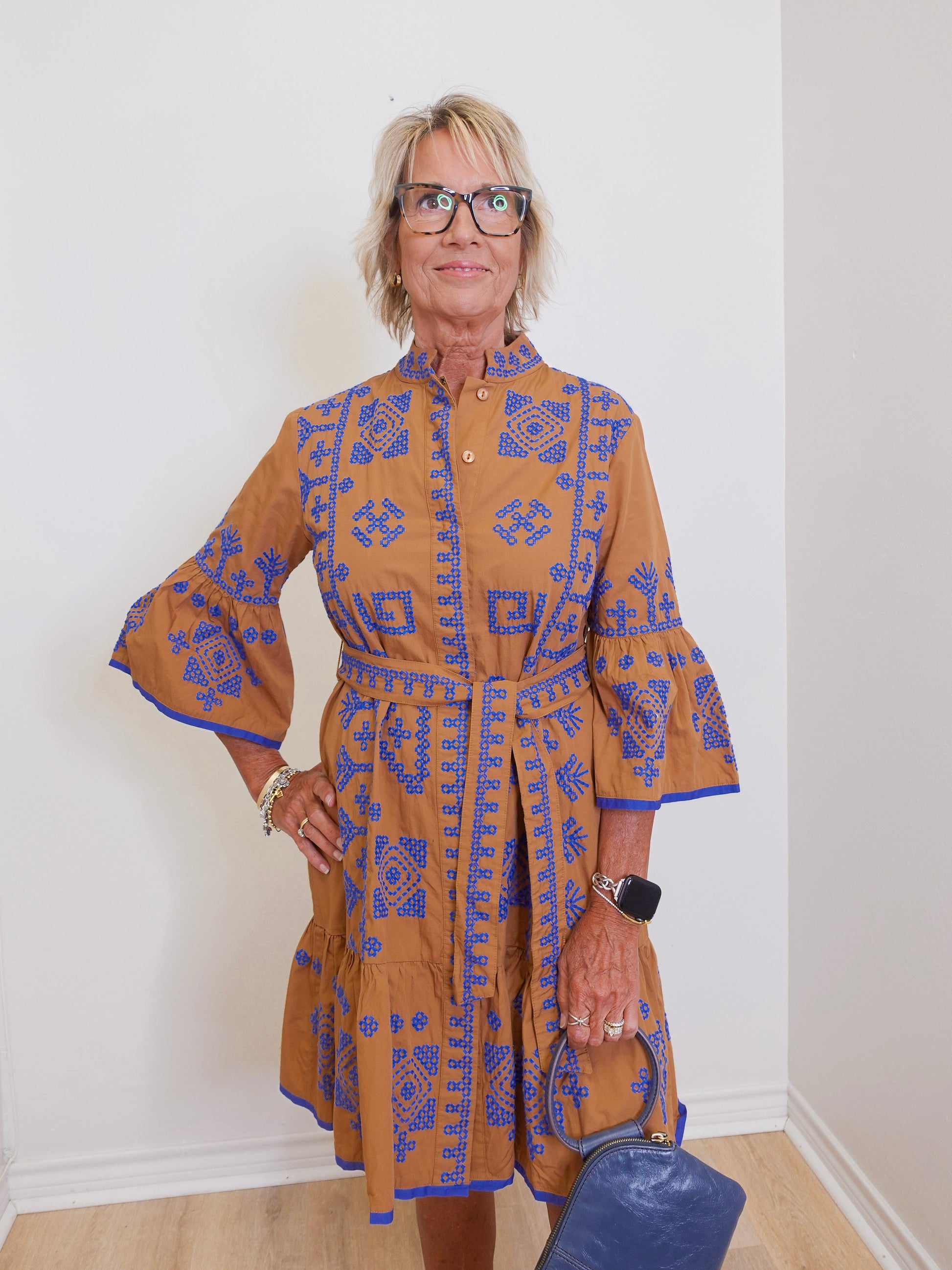 Woman wearing a brown dress with blue patterns against a white wall