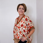 women wearing a beige floral print short sleeve top with black pants against a white wall. 