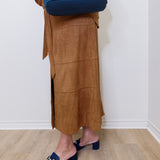 Person wearing a brown suede skirt and blue shoes, holding a blue bag against a white wall.