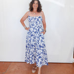 Woman wearing a blue floral dress standing against a white wall.
