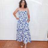 Woman wearing a blue floral dress standing against a white wall.