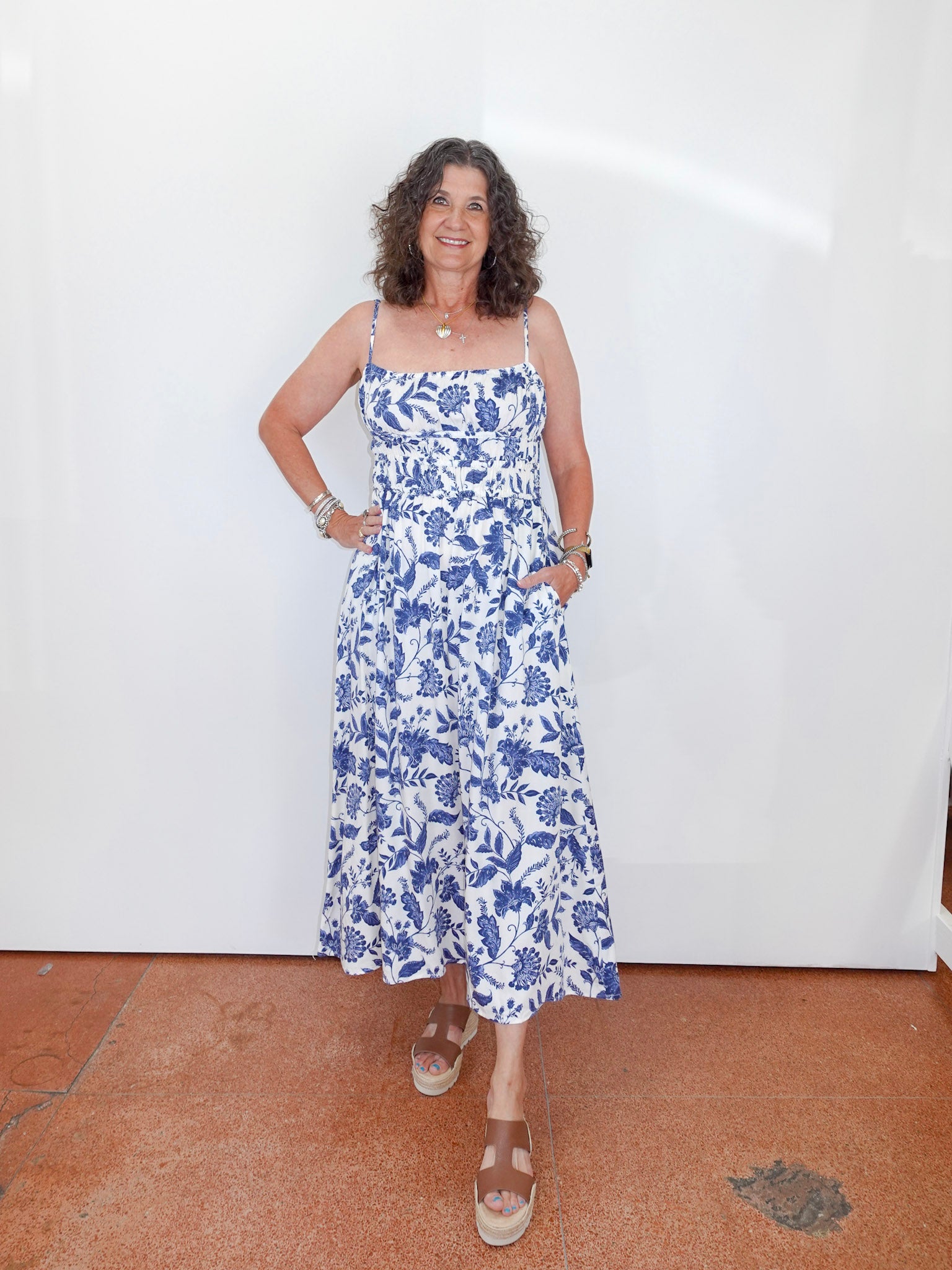 Woman wearing a blue floral dress standing against a white wall.