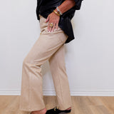 Person wearing a black jacket, beige pants, and black shoes against a white wall.
