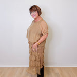 Woman wearing a beige layered dress and black boots against a white wall.
