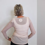 Person wearing a beige long-sleeve top with mesh panels against a white wall