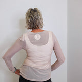 Person wearing a beige long-sleeve top with mesh panels against a white wall