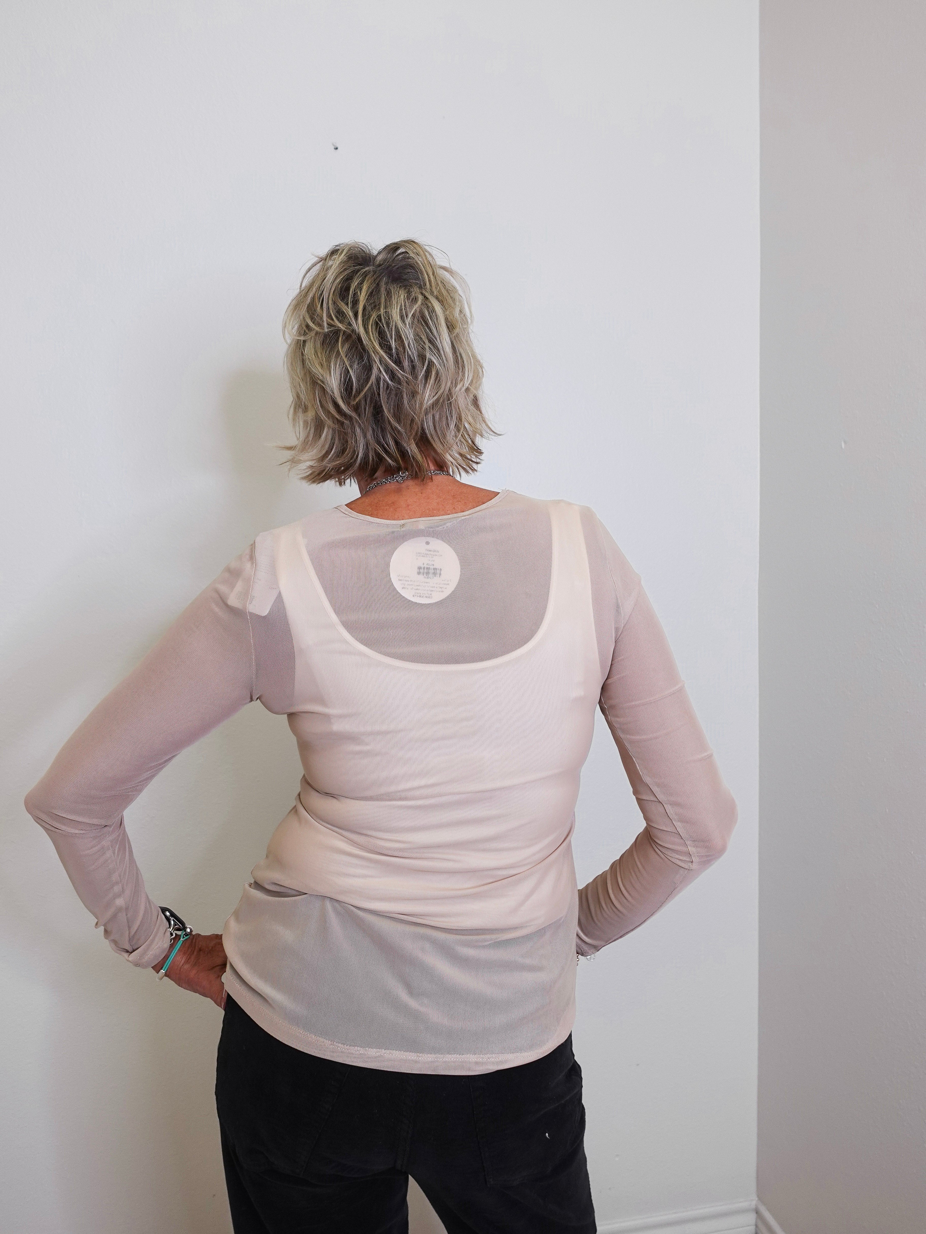 Person wearing a beige long-sleeve top with mesh panels against a white wall
