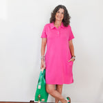 Woman wearing a pink dress holding a green bag against a white wall.