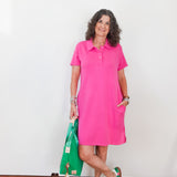 Woman wearing a pink dress holding a green bag against a white wall.