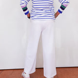 Person wearing a striped shirt and white pants standing on a red floor with a white wall background