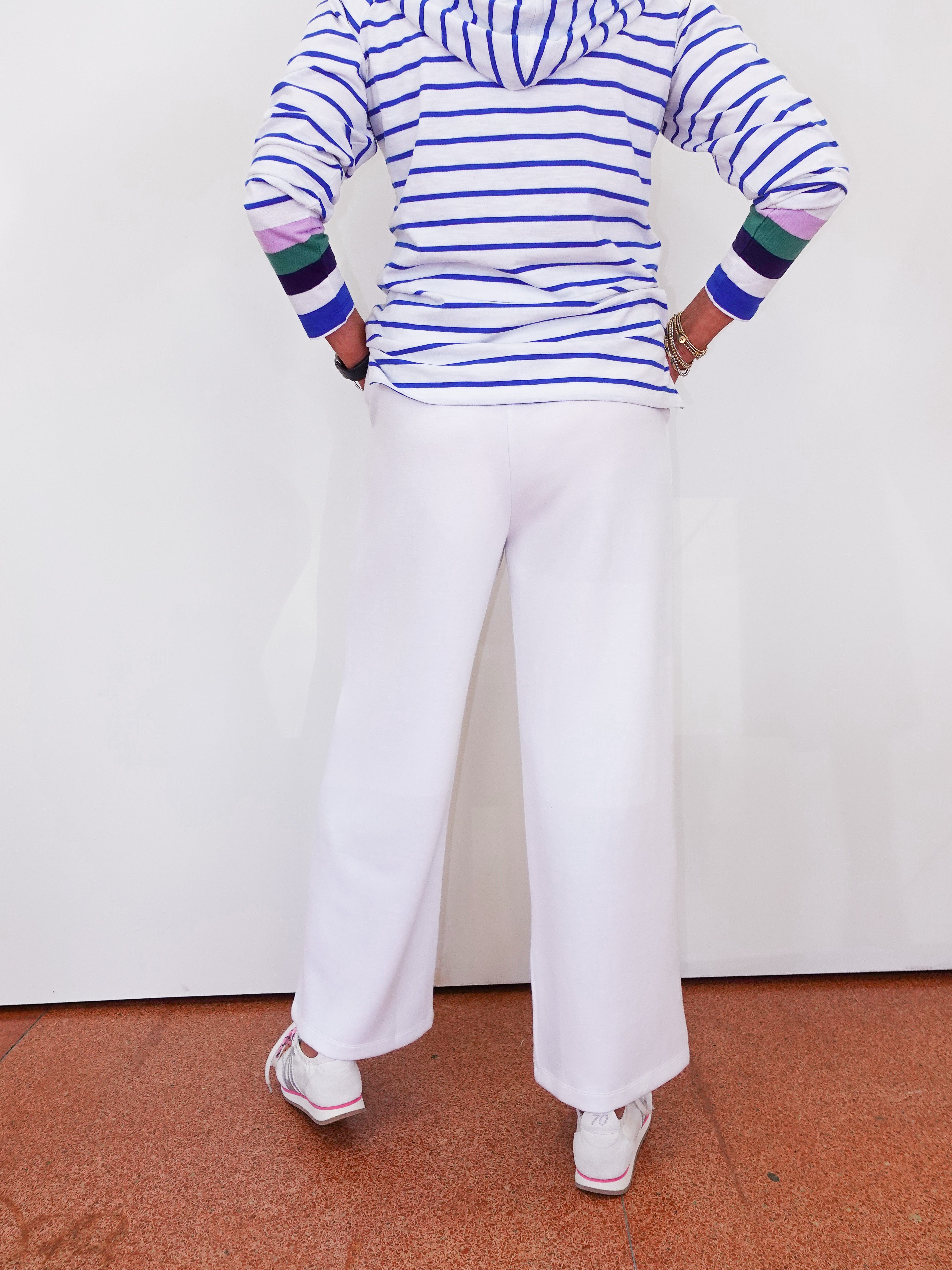 Person wearing a striped shirt and white pants standing on a red floor with a white wall background