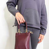 Person holding a maroon handbag against a plain background