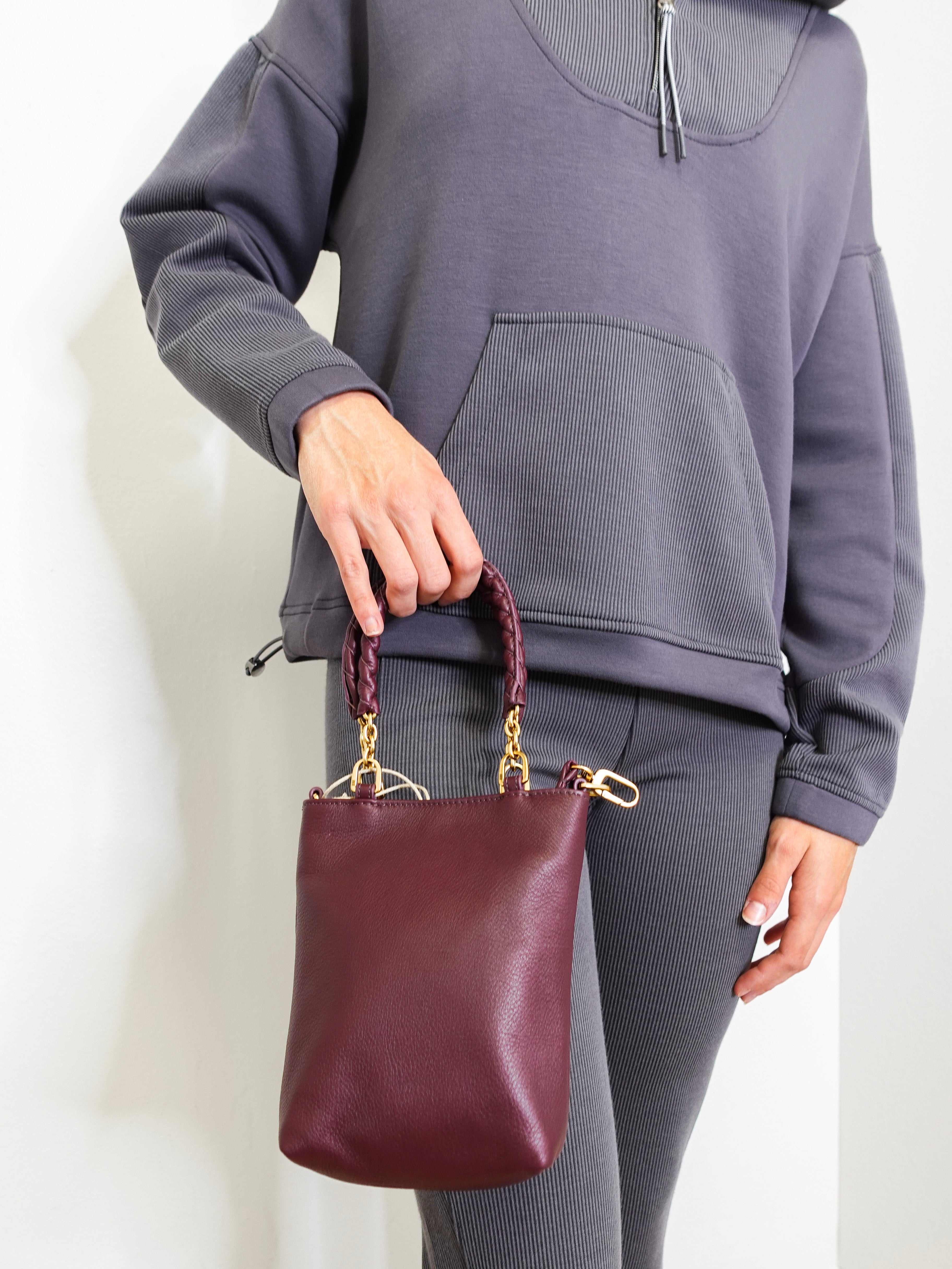 Person holding a maroon handbag against a plain background