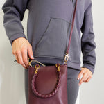Person holding a maroon leather handbag with gold accents against a plain background