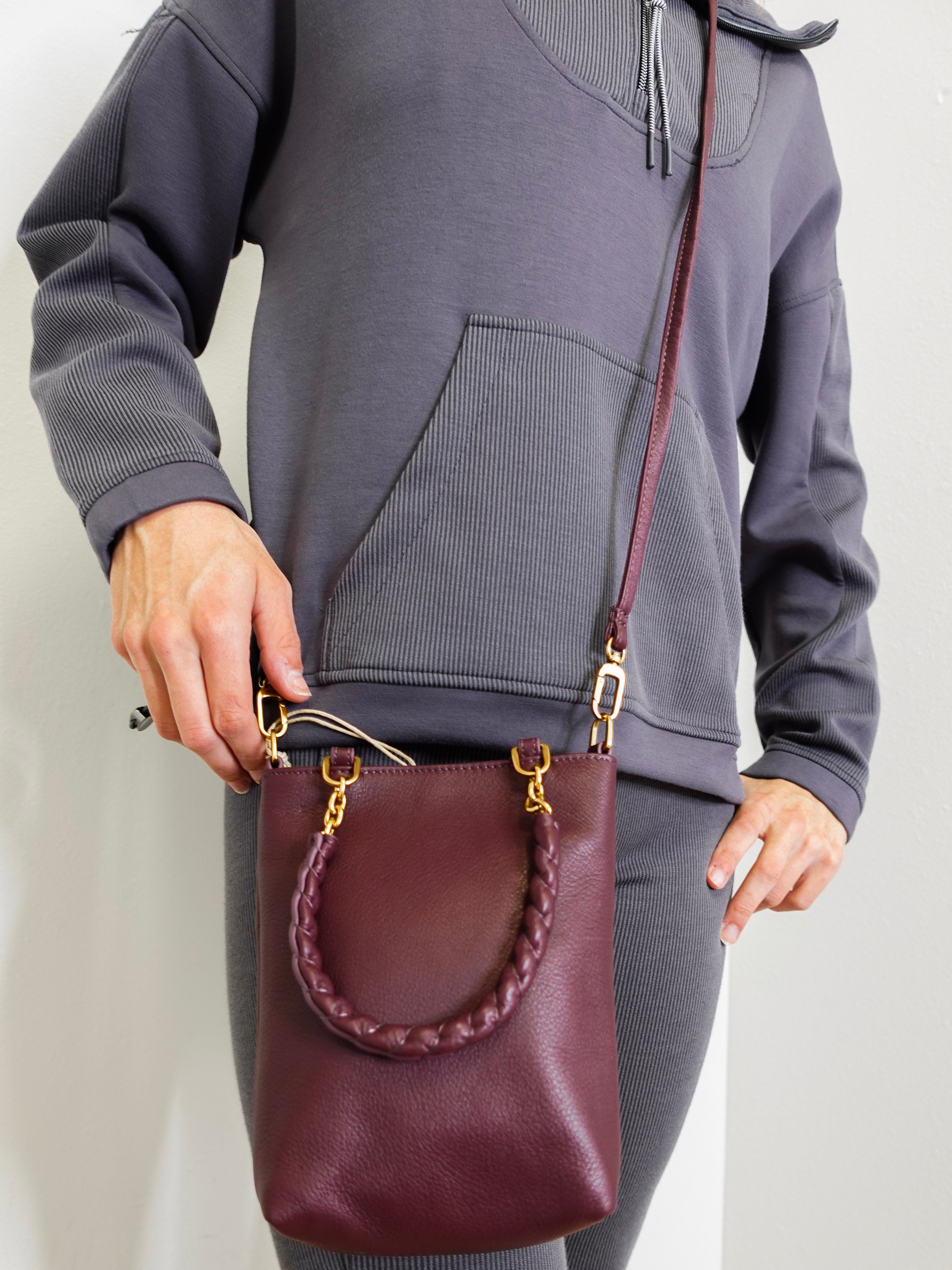 Person holding a maroon leather handbag with gold accents against a plain background