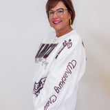 Woman wearing a white sweatshirt with brown text and graphics against a plain background