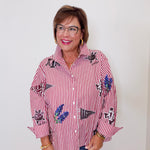 Woman wearing a red and white striped shirt with floral patterns, standing against a plain background.