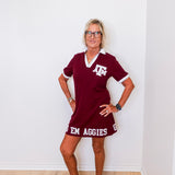 Woman wearing a maroon dress with 'Texas A&M Aggies' text against a white wall.