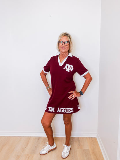 Woman wearing a maroon dress with 'Texas A&M Aggies' text against a white wall.