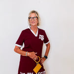 Woman wearing a maroon dress with 'Gig 'Em Aggie' text and a yellow clutch against a white background