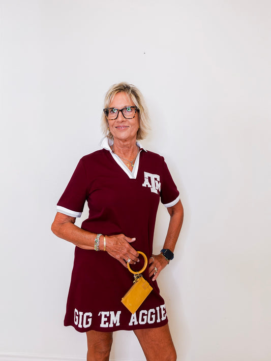 Woman wearing a maroon dress with 'Gig 'Em Aggie' text and a yellow clutch against a white background