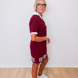 Woman wearing a maroon dress with white accents against a white wall.