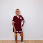 Woman wearing a maroon dress with 'Texas A&M' text against a white wall.