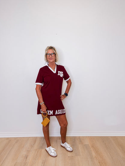 Woman wearing a maroon dress with 'Texas A&M' text against a white wall.