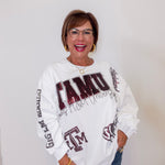 Person wearing a white sweatshirt with ' TAMU' text and graphics on a plain background
