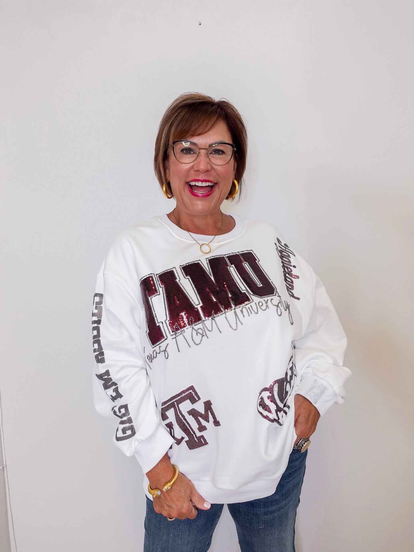 Person wearing a white sweatshirt with ' TAMU' text and graphics on a plain background