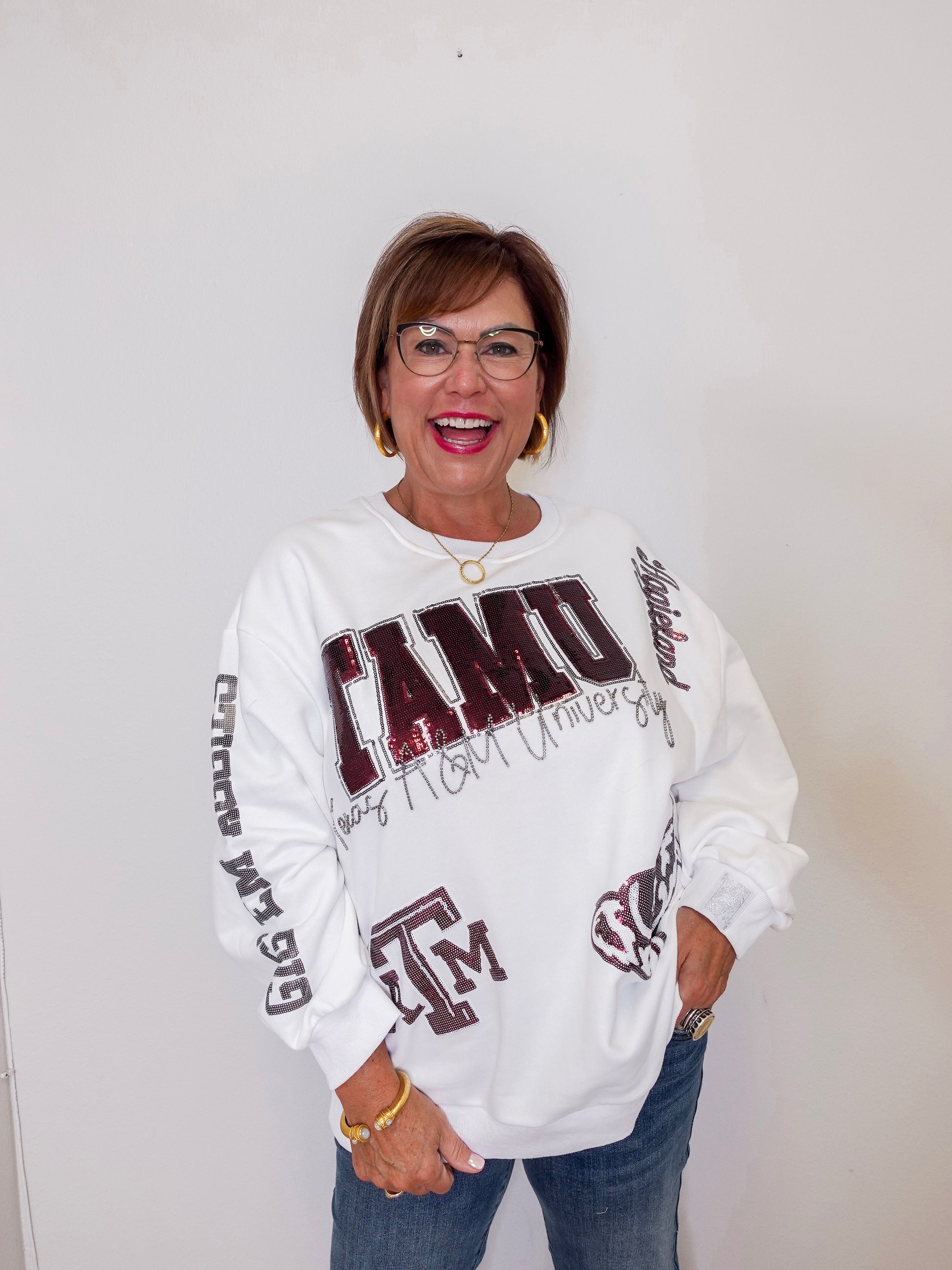 Person wearing a white sweatshirt with ' TAMU' text and graphics on a plain background