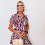 Woman wearing a patterned dress and holding a beige handbag against a white background