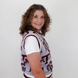 Woman wearing a patterned top and white pants against a plain background